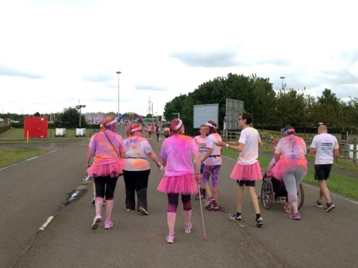 Finish in site! Typical of her, Deb’s tutu is tucked in her trousers! Left to right: Sare, Giggler, Angie, Matthew, Sharon, Lewis, Deb pushing me in Wilma, Adam *Photo courtesy of Jazz & team*